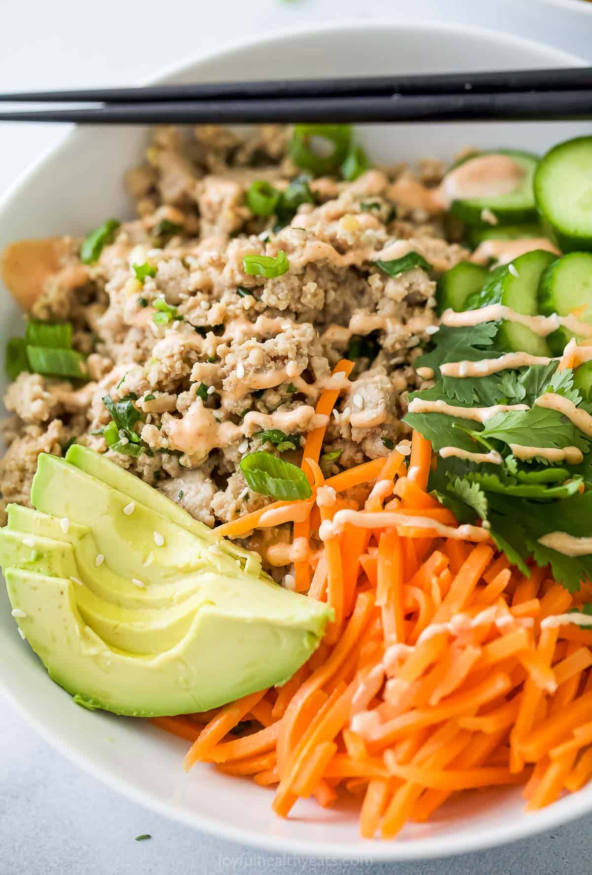 Closeup of banh mi bowl topped with avocado, pickled carrots, and spicy mayo