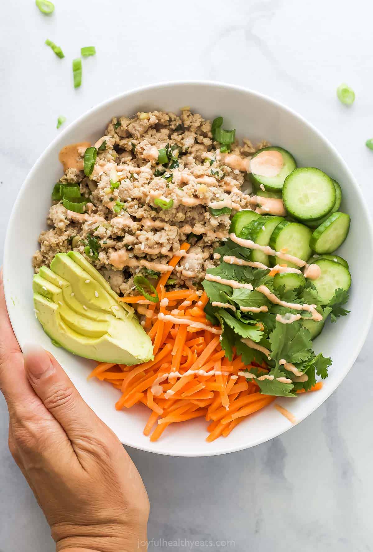 Overhead view of hand holding banh mi bowl with ground turkey and spicy mayo