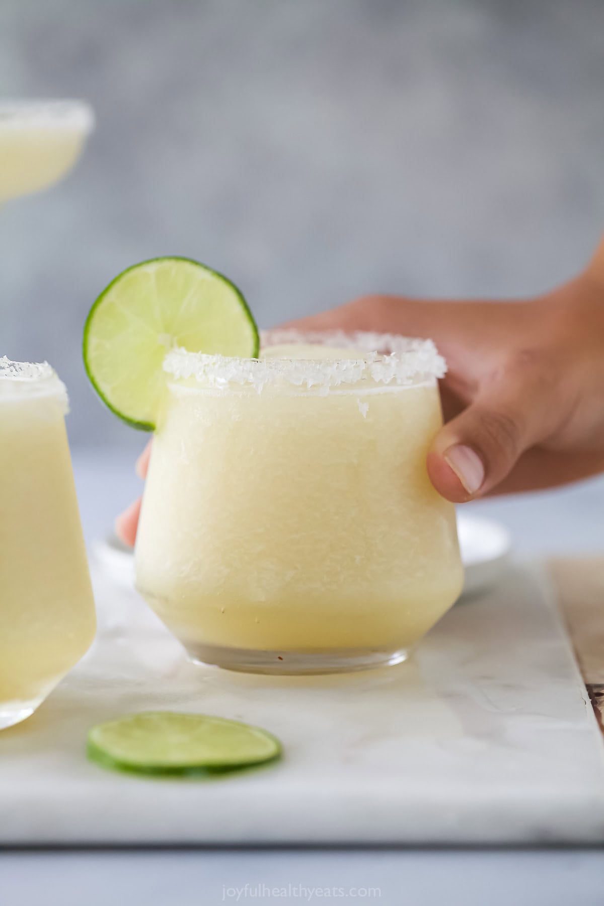 Hand holding frozen margarita in glass with salted rim and lime wheel