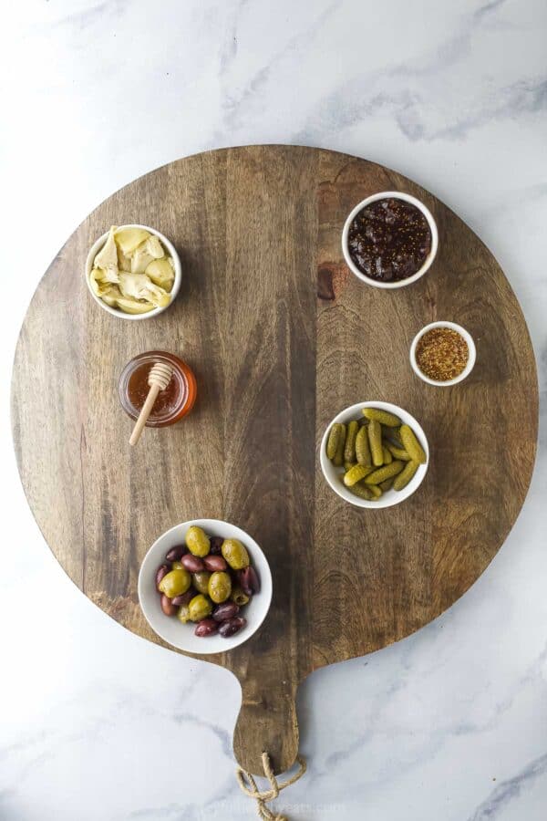 Overhead view of olives, honey, marinated olives, and other extras in bowls set on round wooden board