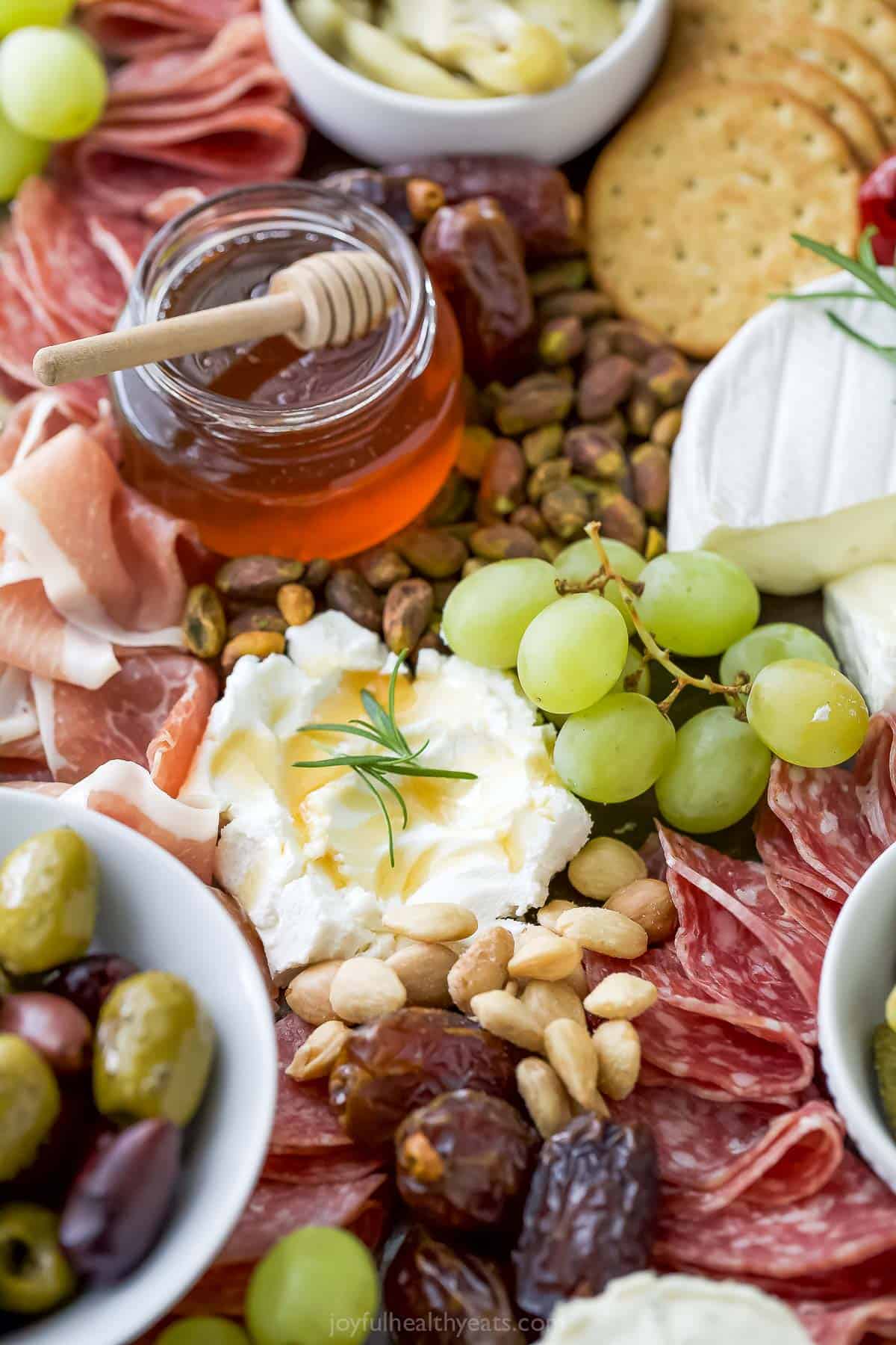 Closeup of charcuterie board with nuts, fruit, honey, and cheeses