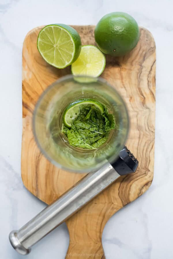 This Nojito recipe has everything you love about the original, minus the alcohol! Fresh mint, lime and sparkling water make it so refreshing. Overhead view of mint and lime muddled in glass