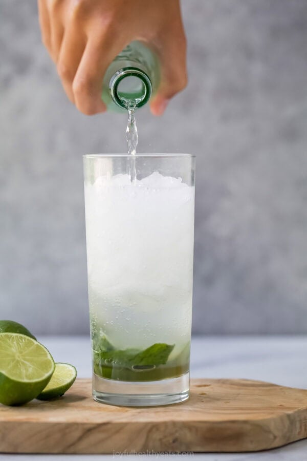 This Nojito recipe has everything you love about the original, minus the alcohol! Fresh mint, lime and sparkling water make it so refreshing. Pouring sparkling water into glass for mojito mocktail