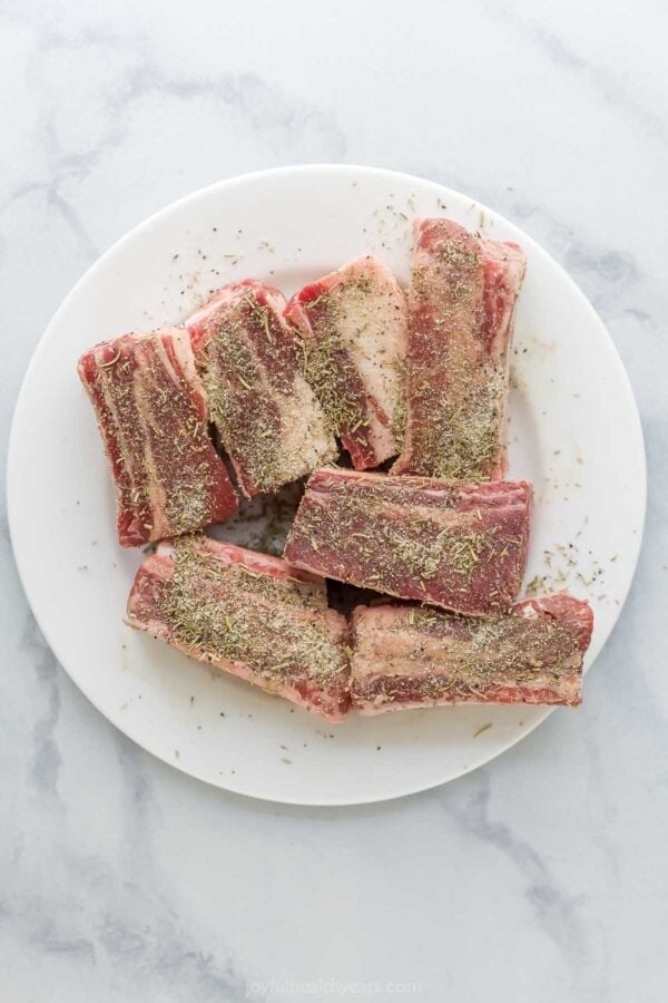 Overhead view of seasoned raw short ribs on plate