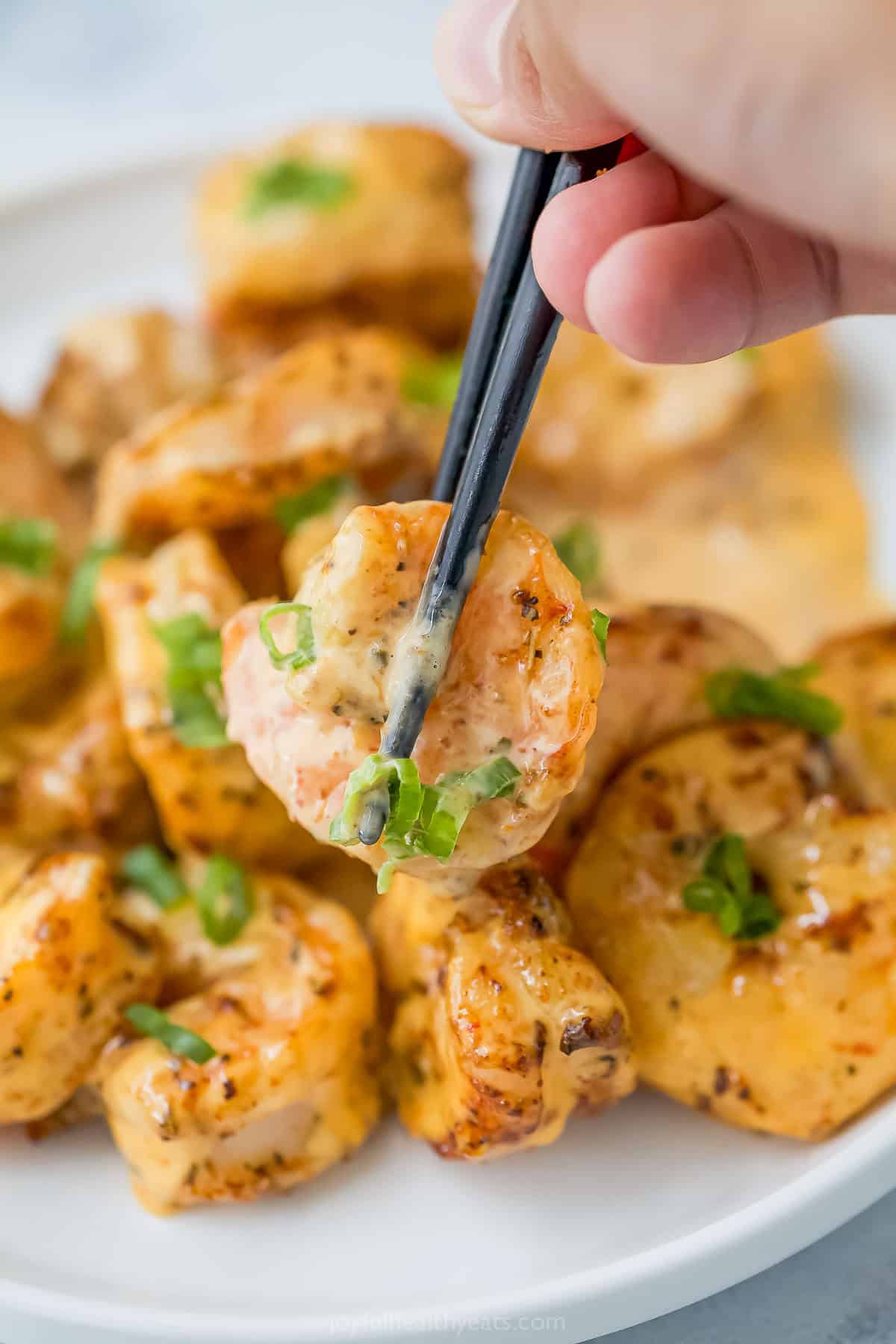 The air fryer makes this crispy Bang Bang Shrimp recipe super easy and lighter, and a creamy, spicy sauce makes it irresistible! Chopsticks picking up bang bang shrimp from plate