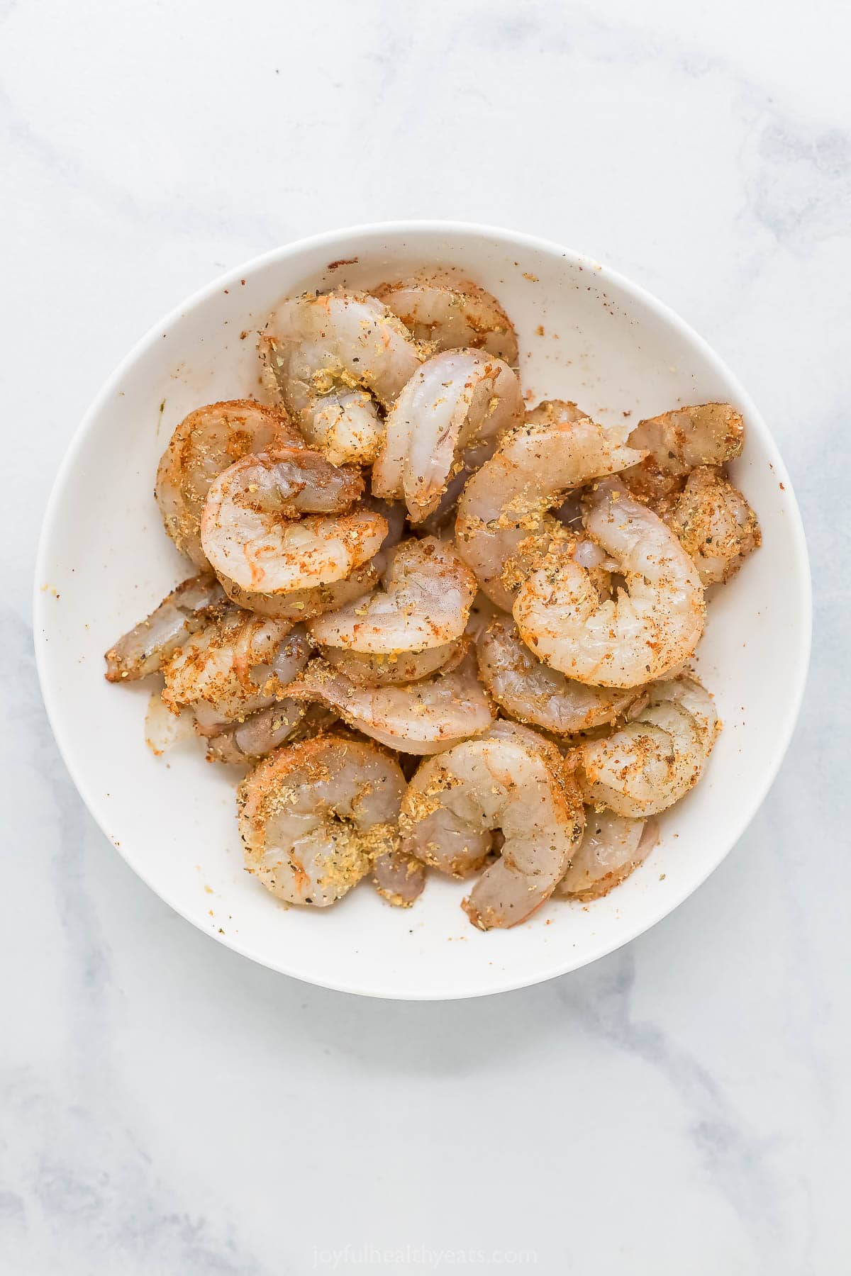 The air fryer makes this crispy Bang Bang Shrimp recipe super easy and lighter, and a creamy, spicy sauce makes it irresistible! Overhead view of uncooked shrimp in bowl with seasonings