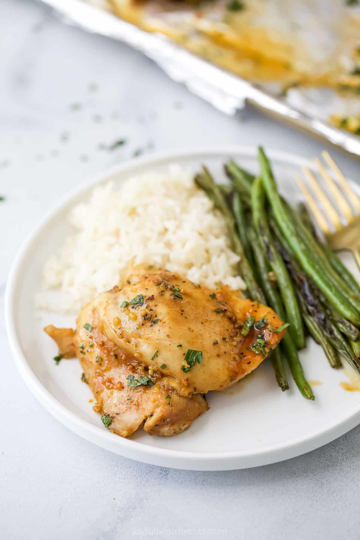 Honey garlic slow cooker chicken thigh on plate with roasted green beans and white rice