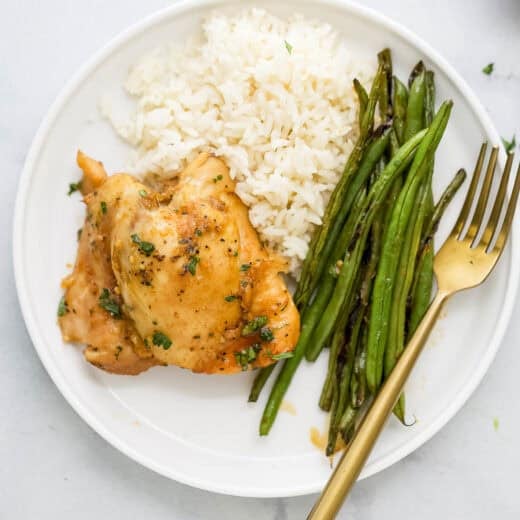Overhead view of slow cooker chicken thigh on plate with green beans and rice