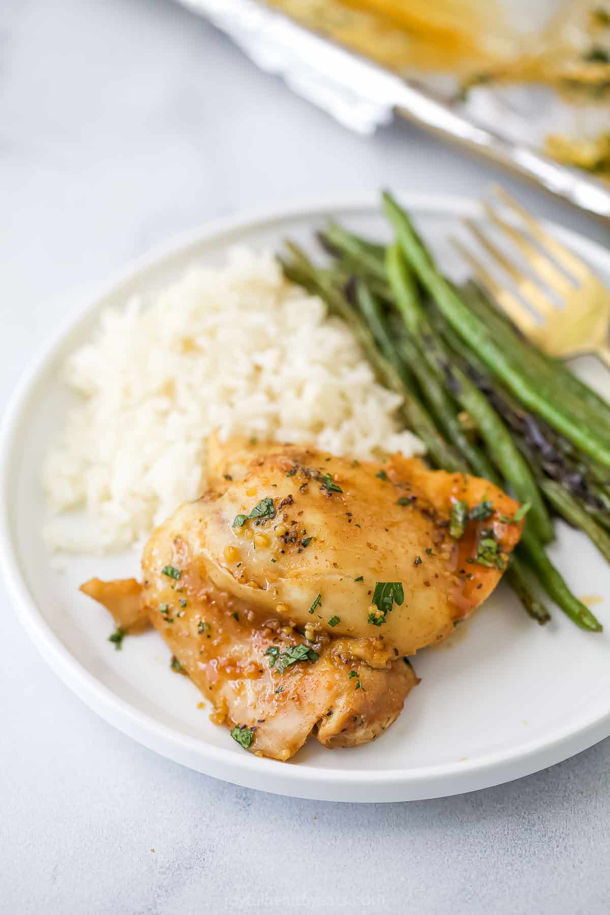 Honey garlic slow cooker chicken thigh on plate with roasted green beans and white rice