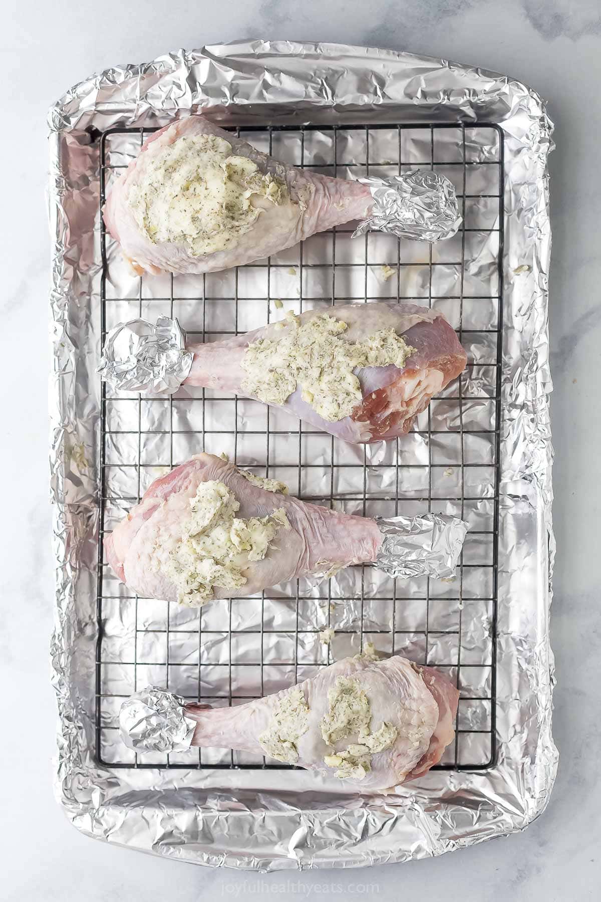 This Garlic Herb Roasted Turkey Leg recipe is juicy and succulent, with an herbed garlic butter rub that adds SO much flavor. The best! Raw turkey legs rubbed with butter on wire rack set on sheet pan.