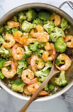 Skillet of honey garlic shrimp and broccoli with wooden spoon.