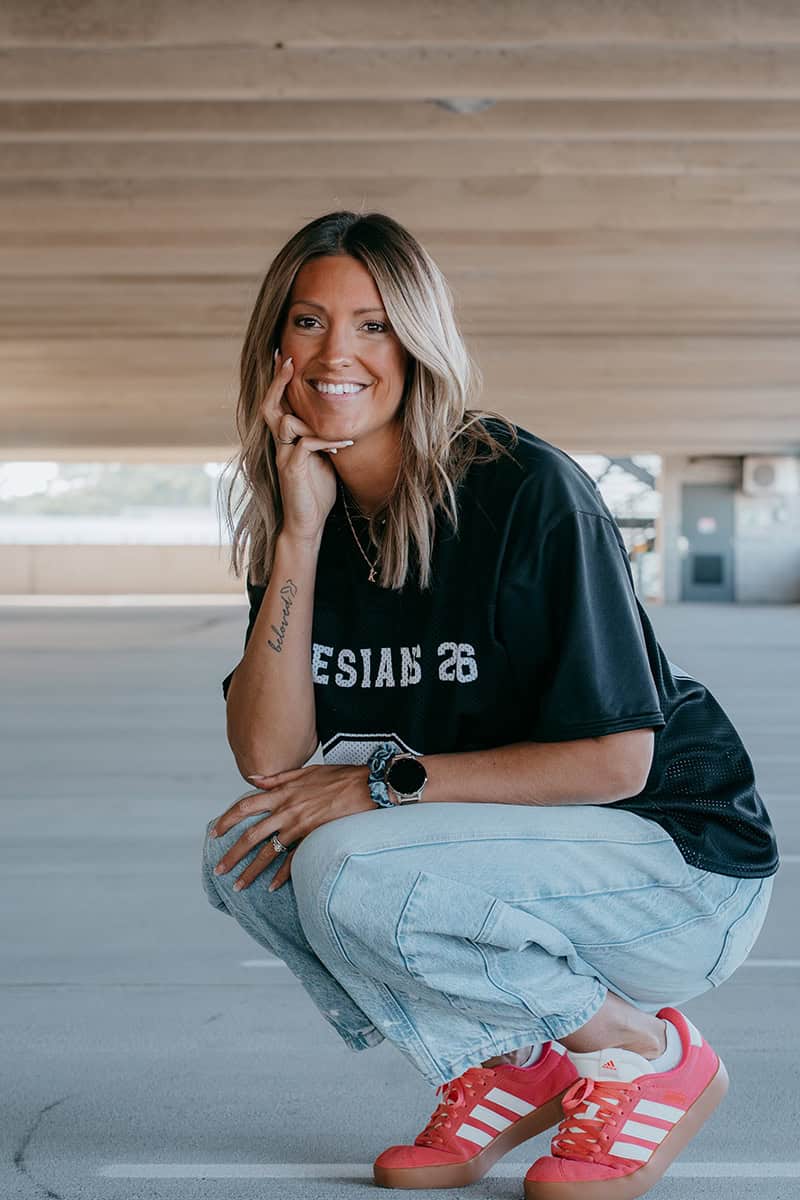 Photo of Krista Rollins in jeans, a dark blue t-shirt and orange sneakers.