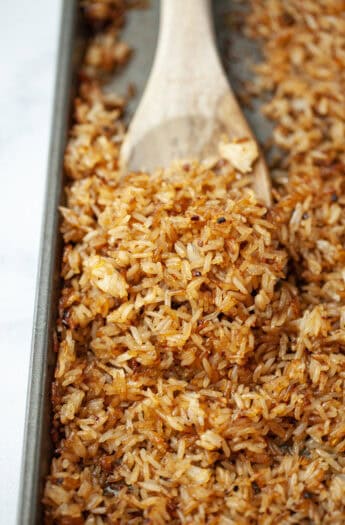 Wooden spoon scooping crispy rice from sheet pan.
