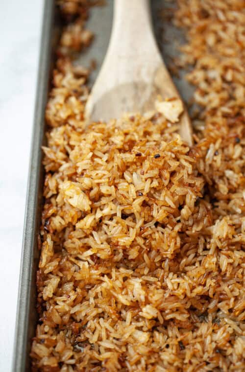 Wooden spoon scooping crispy rice from sheet pan.
