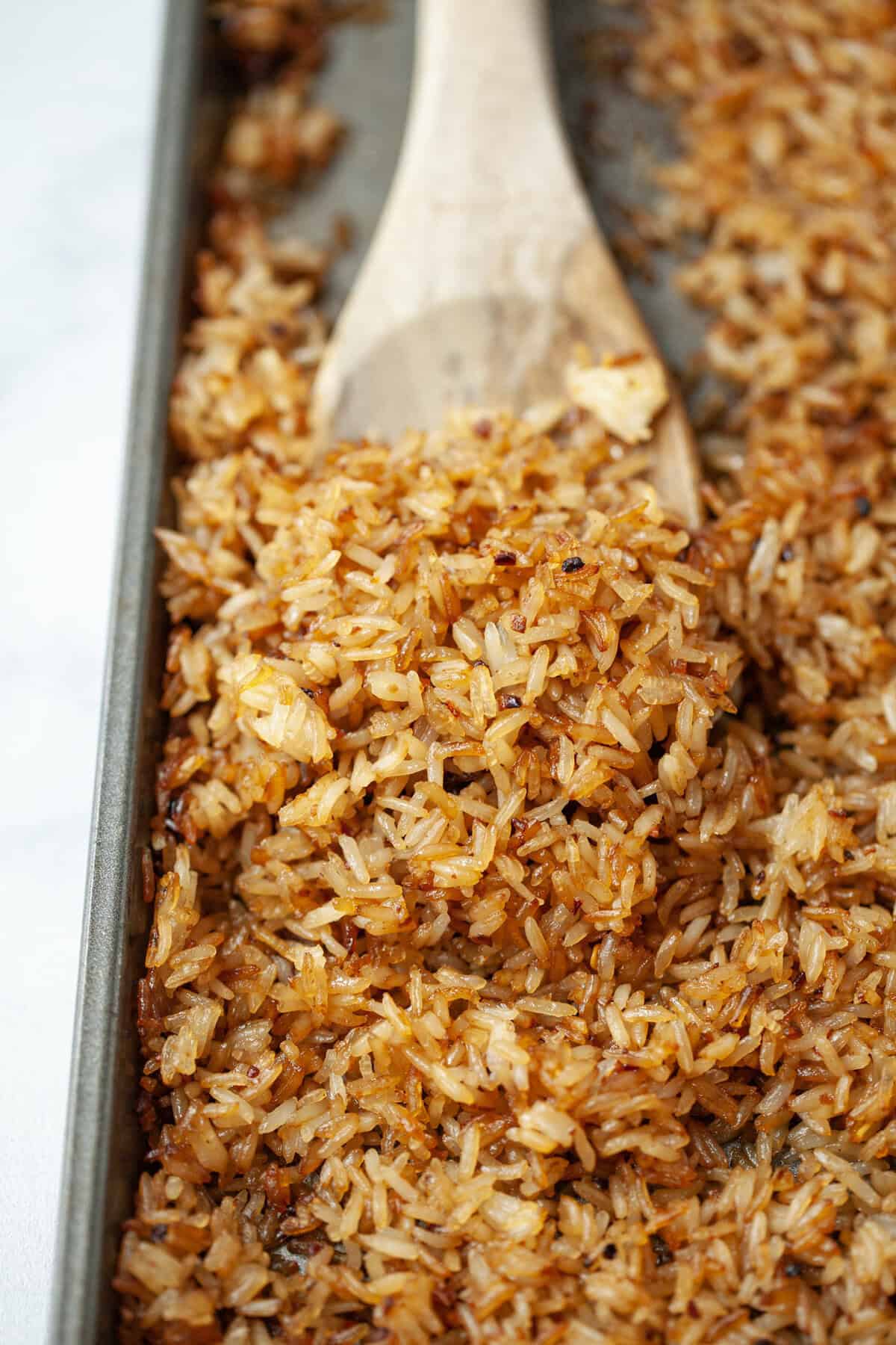This viral TikTok sheet pan crispy rice is tossed in savory sauce and baked until golden for the perfect addition to salads, bowls and more! Wooden spoon scooping crispy rice from sheet pan.