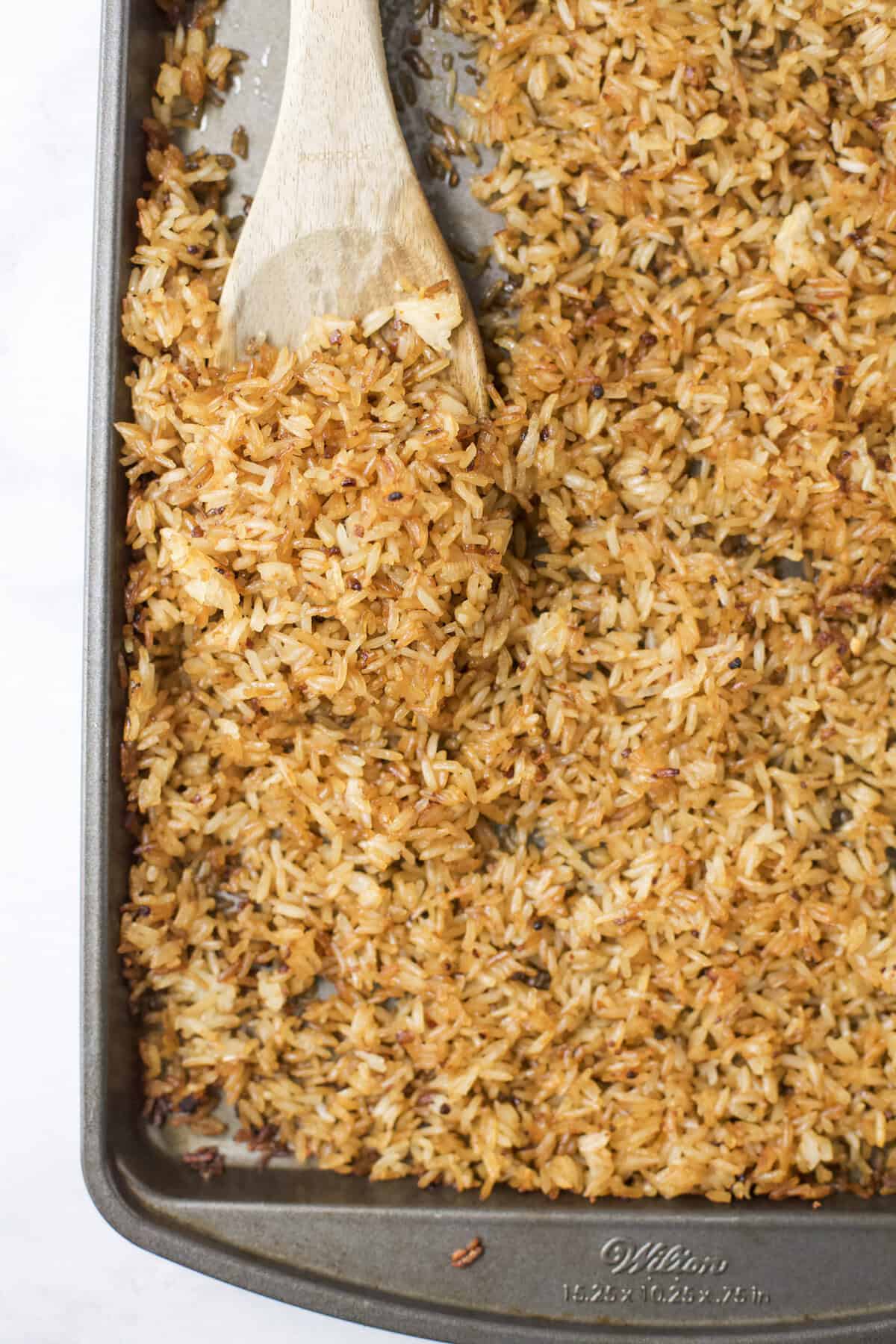 This viral TikTok sheet pan crispy rice is tossed in savory sauce and baked until golden for the perfect addition to salads, bowls and more! Crispy rice being scooped from sheet pan with wooden spoon.