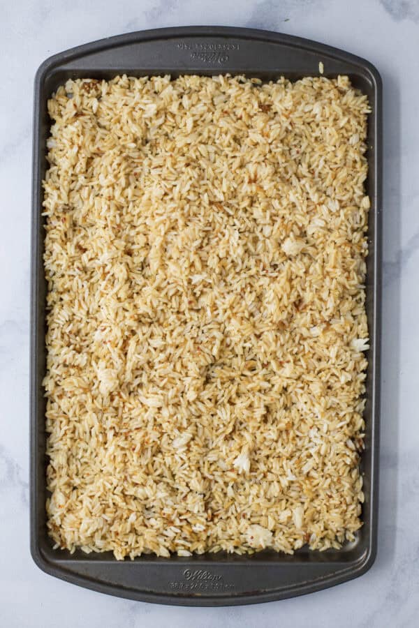 This viral TikTok sheet pan crispy rice is tossed in savory sauce and baked until golden for the perfect addition to salads, bowls and more! Rice spread onto sheet pan.