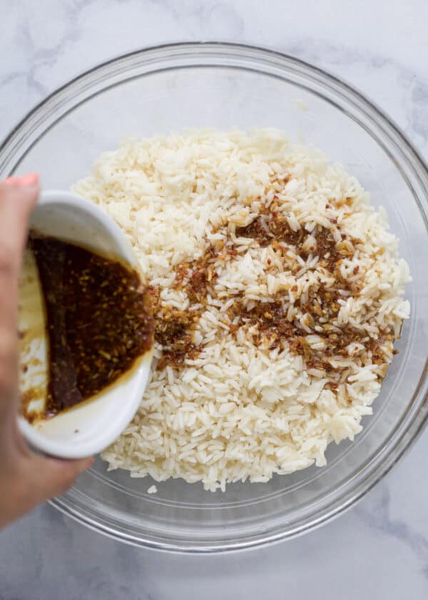 This viral TikTok sheet pan crispy rice is tossed in savory sauce and baked until golden for the perfect addition to salads, bowls and more! Pouring sauce over bowl of jasmine rice.