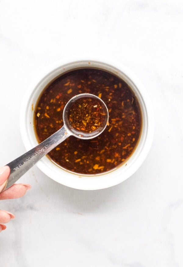 This viral TikTok sheet pan crispy rice is tossed in savory sauce and baked until golden for the perfect addition to salads, bowls and more! Spoonful of chili crisp sauce held over bowl.