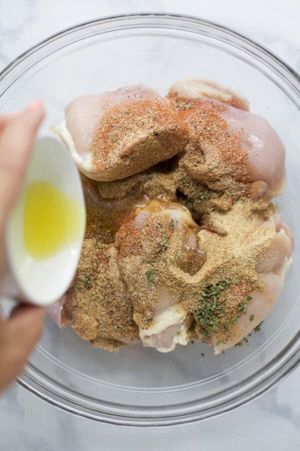 Pouring oil into bowl of raw chicken thighs and seasonings.