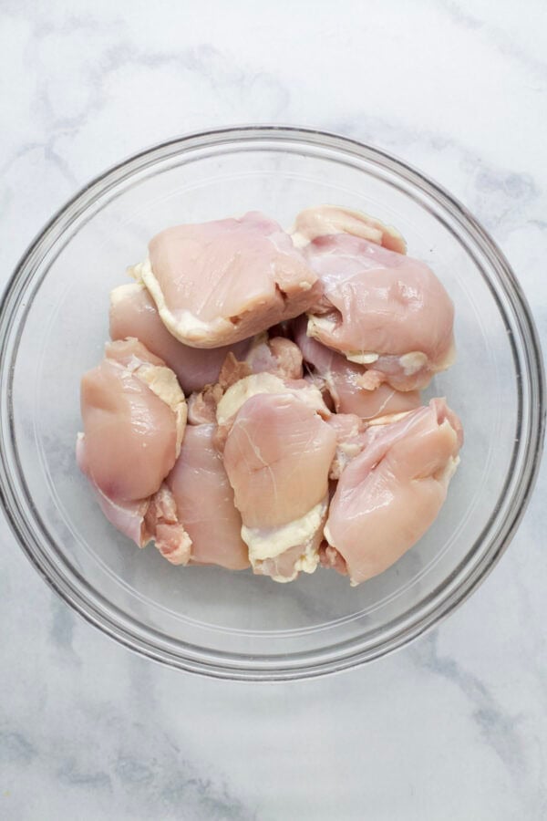 Raw chicken thighs in glass bowl.