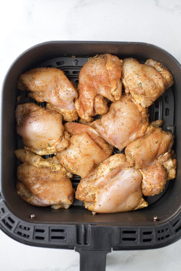 Raw chicken thighs arranged in air fryer basket.