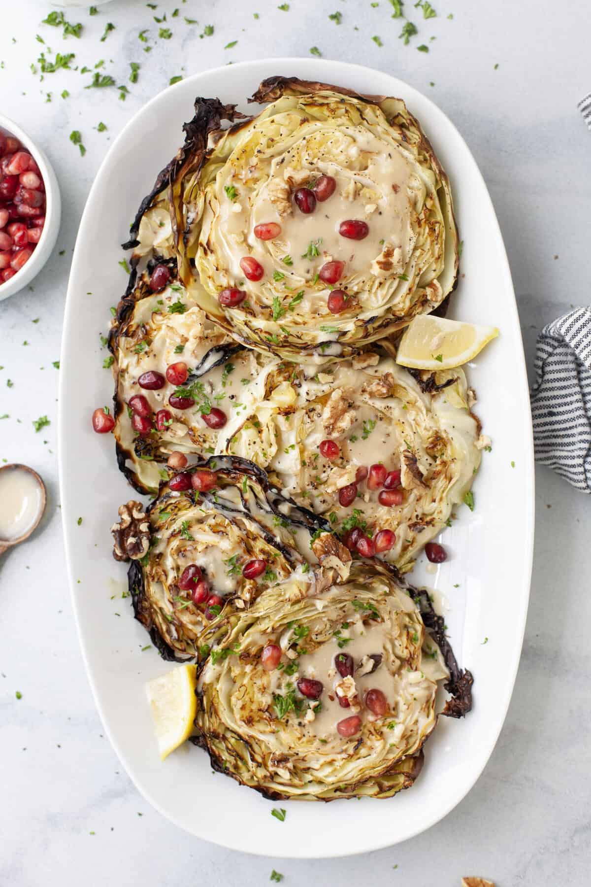 Roasted cabbage steaks on platter with maple tahini sauce and pomegranate arils.