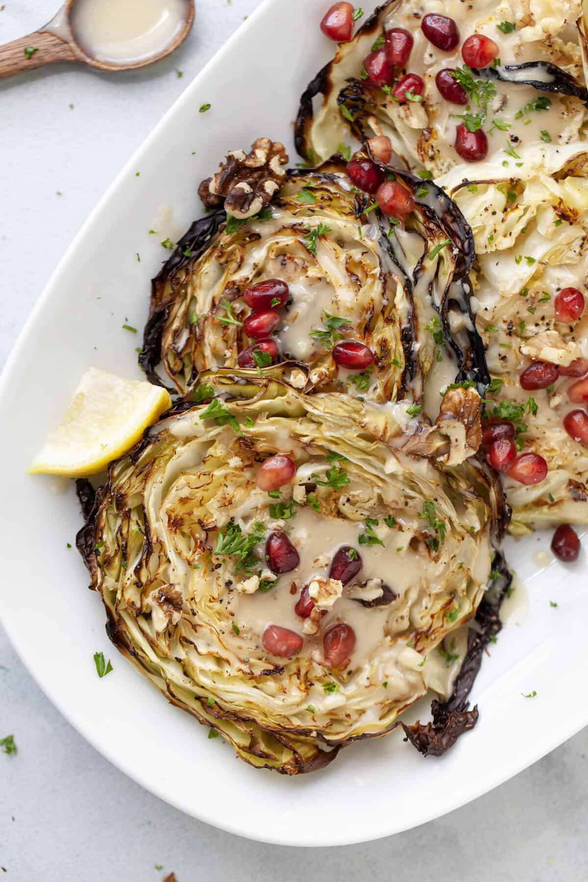 Serving platter of blistered cabbage steaks with pomegranate and tahini.