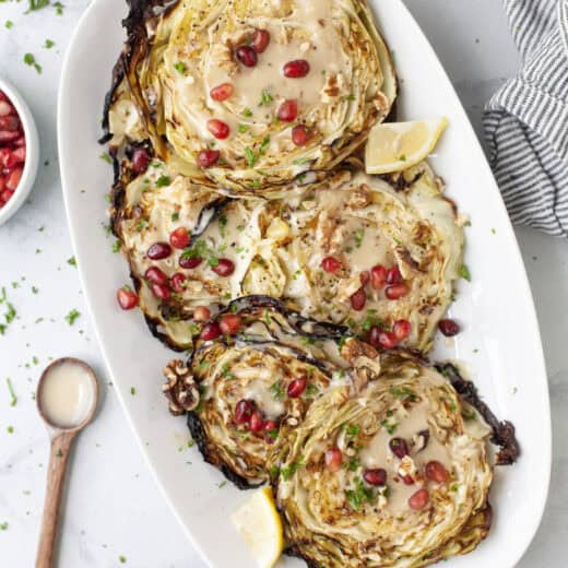 Blistered cabbage steaks on platter with maple tahini sauce, walnuts, and pomegranate arils.