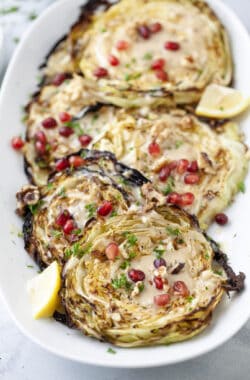 Blistered cabbage steaks on platter with tahini sauce and pomegranate arils.
