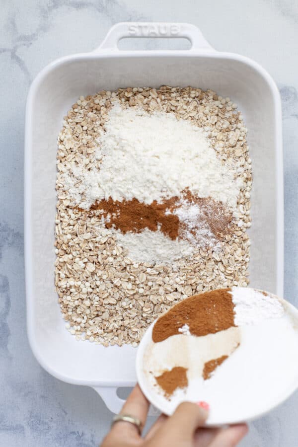 Adding dry ingredients to baking dish with old-fashioned oats.