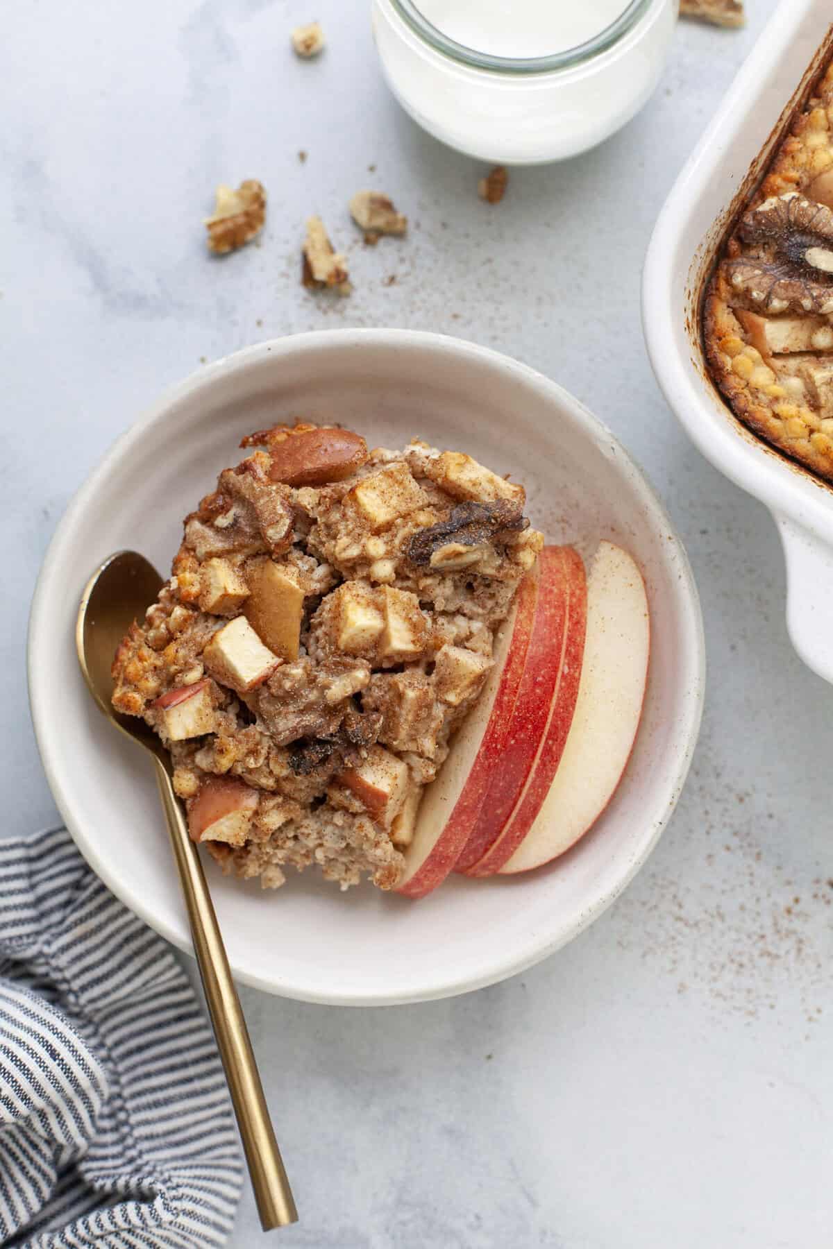 Cinnamon baked apple oatmeal in bowl with apple slices and spoon.