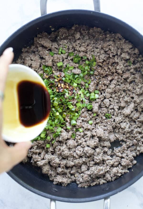 Pouring tamari into pan of ground beef and green onions.