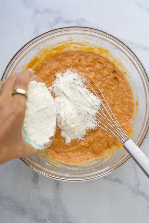 Pouring dry ingredients into wet ingredients for pumpkin protein muffins.