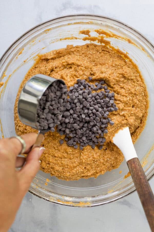 Pouring mini chocolate chips into protein pumpkin muffin batter.